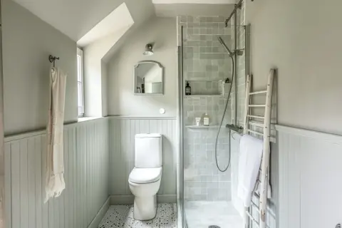 Douche, WC et lavabo dans une petite salle de bain 3m2. Un style épuré et fonctionnel avec des carreaux gris et un mur lambrissé.