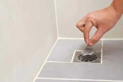 Main d'une personne retirant des cheveux du siphon pour déboucher la douche.