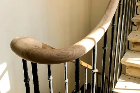 Courbe élégante d'une main courante en bois sur une volée d'escalier aux barreaux de fer forgé, baignée de lumière.