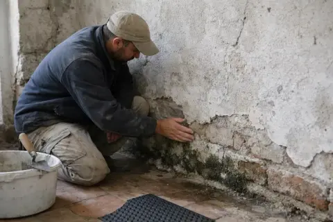 Un homme examine un mur dégradé par l'humidité, signe de condensation dans la maison.