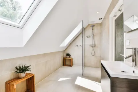 Élégante salle de bain sous comble avec douche moderne, lavabo design et puits de lumière.