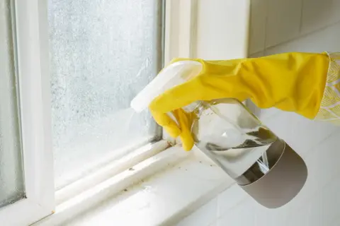 Main jaune pulvérisant un produit sur une fenêtre en aluminium sale après un chantier.