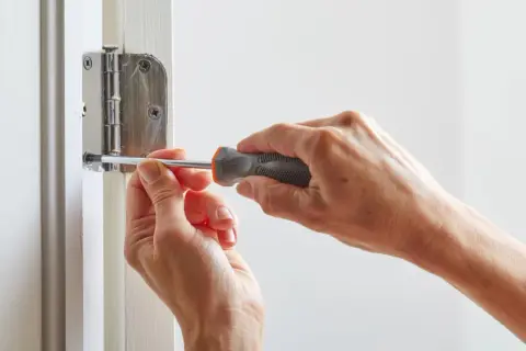 Mains serrant une vis avec un tournevis pour réparer une porte qui grince.