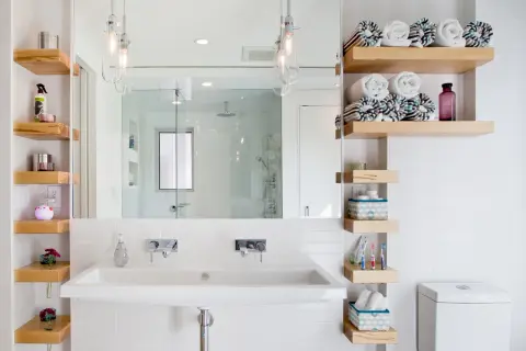 Salle de bain petite surface : lavabo double, étagères en bois flotté, miroir, douche vitrée et toilettes. Idée déco fonctionnelle.