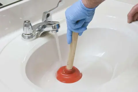 Main tenant utilise une ventouse pour déboucher un lavabo. L'eau s'accumule, signe d'un lavabo bouché.