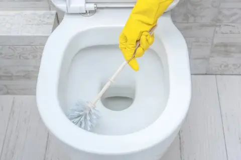 Main jaune nettoyant le tartre WC avec une brosse.