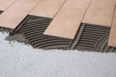 Pose de carrelage droit ou décalé sur lit de mortier frais. Les carreaux beiges sont appliqués sur un support en béton.