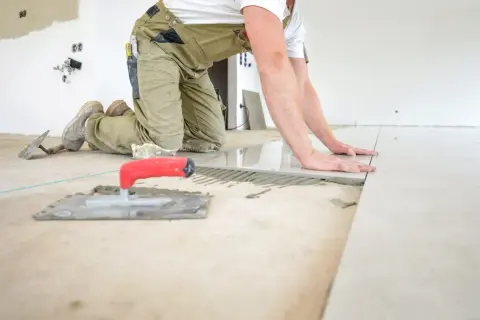 Pose d'un carrelage au sol, le carreleur ajuste la pose pour une épaisseur parfaite. Outils de pose à proximité.