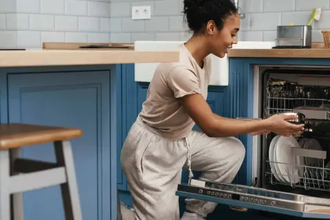 Une femme charge son lave-vaisselle encastrable. Elle place une casserole dans le panier inférieur.