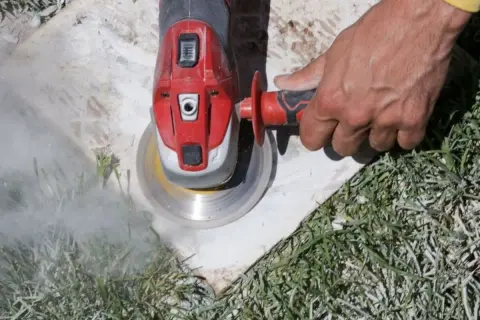 Main d'un ouvrier utilisant une meuleuse pour enlever ciment colle sous carrelage. Nuage de poussière.