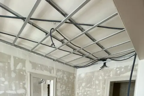 Structure métallique pour faire un faux plafond, avec des câbles électriques en cours d'installation. Les murs sont en chantier.