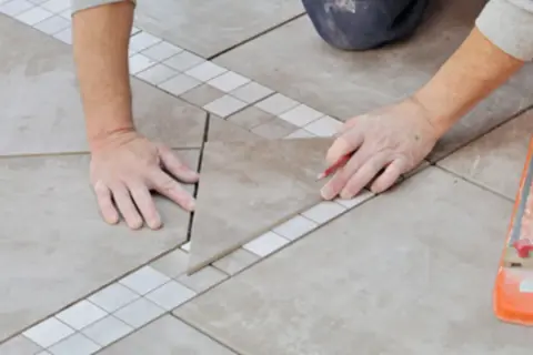 Un carreleur prépare le plan de pose du carrelage, marquant une pièce avec un crayon.