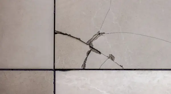 Gros plan sur un carrelage de sol beige avec une fissure importante. Il faut réparer cette fissure pour éviter qu'elle ne s'aggrave.