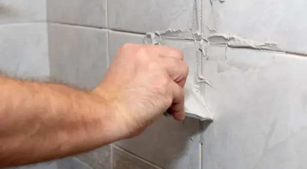 Main tenant utilise une spatule pour refaire le joint du carrelage mural.