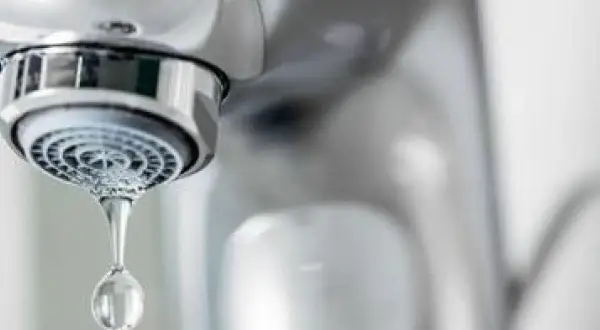 Goutte d'eau tombant d'un robinet qui goutte. Le chrome brillant du robinet contraste avec la goutte d'eau transparente.