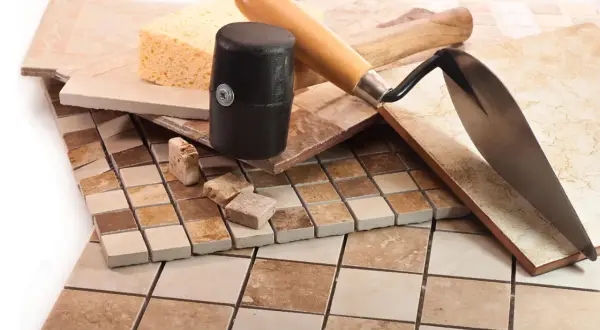 Diverses carreaux de céramique, une éponge, un maillet et une truelle, prêts pour une pose mosaïque sol.