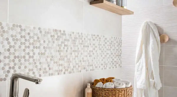 Détail d'une salle de bain moderne avec une bande de pose de faïence en mosaïque hexagonale. Un panier de serviettes et un peignoir blanc complètent la scène.