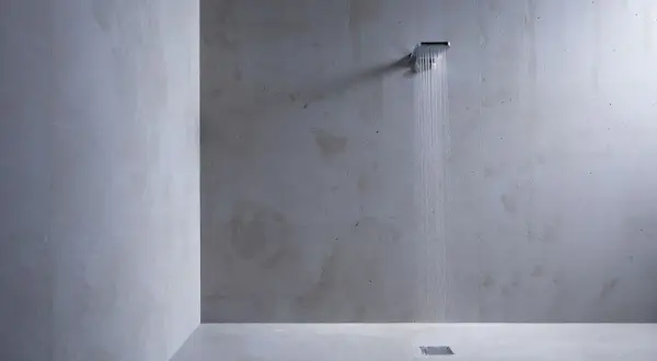 Douche moderne au design épuré, avec un mur et un sol en béton ciré. L'eau coule d'une douchette carrée, créant une ambiance zen.