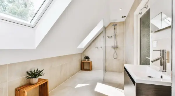 Élégante salle de bain sous comble avec douche moderne, lavabo design et puits de lumière.