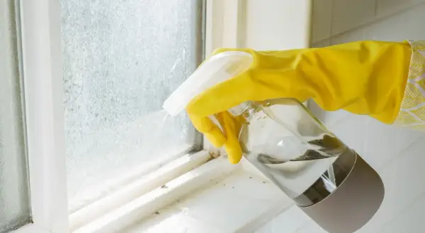 Main jaune pulvérisant un produit sur une fenêtre en aluminium sale après un chantier.