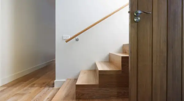 Escalier en bois clair, parfait pour un entretien facile. Une porte en bois sombre s'ouvre sur la cage d'escalier.