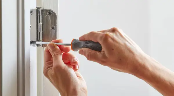 Mains serrant une vis avec un tournevis pour réparer une porte qui grince.
