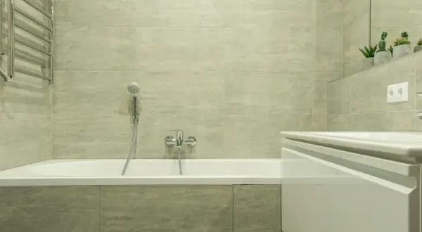 Salle de bain moderne avec baignoire blanche, carrelage gris clair et porte-serviettes chromé. Idéal pour apprendre comment rénover une baignoire.