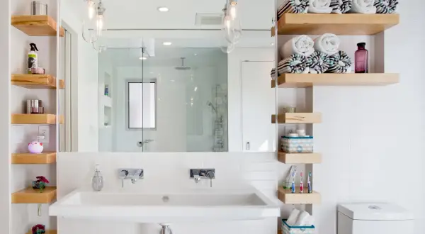 Salle de bain petite surface : lavabo double, étagères en bois flotté, miroir, douche vitrée et toilettes. Idée déco fonctionnelle.