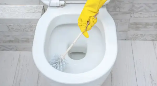 Main jaune nettoyant le tartre WC avec une brosse.