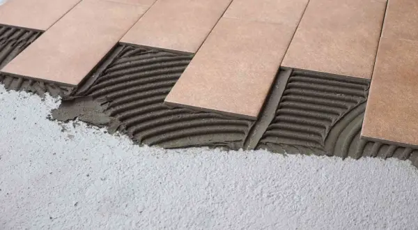 Pose de carrelage droit ou décalé sur lit de mortier frais. Les carreaux beiges sont appliqués sur un support en béton.