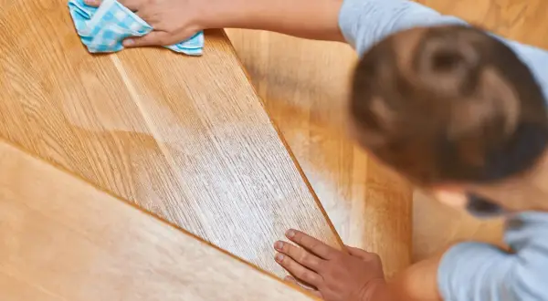Une personne nettoie un escalier en bois encrassé avec un chiffon bleu à carreaux.