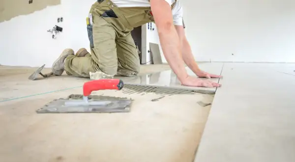 Pose d'un carrelage au sol, le carreleur ajuste la pose pour une épaisseur parfaite. Outils de pose à proximité.