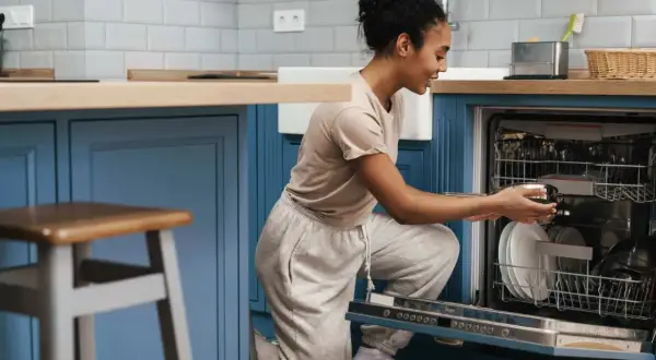 Une femme charge son lave-vaisselle encastrable. Elle place une casserole dans le panier inférieur.