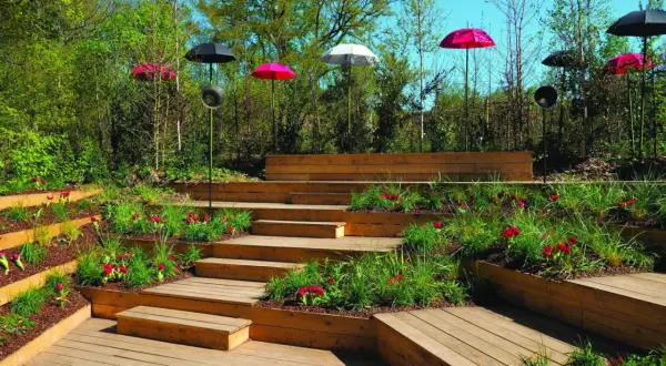 Escalier extérieur en bois avec des parterres de fleurs et des parasols colorés. La norme hauteur marche escalier extérieur est respectée pour un accès sûr.