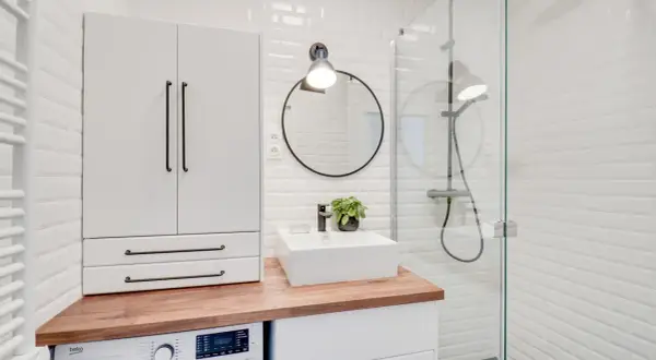 Coin buanderie dans salle de bain moderne avec machine à laver, lavabo, miroir rond et douche vitrée.