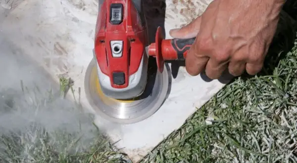 Main d'un ouvrier utilisant une meuleuse pour enlever ciment colle sous carrelage. Nuage de poussière.