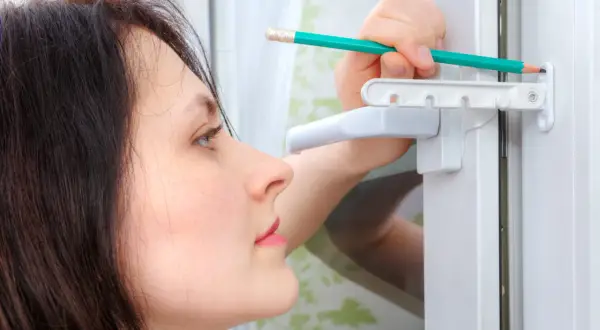 Une femme ajuste une vis de réglage sur une fenêtre PVC avec un crayon.