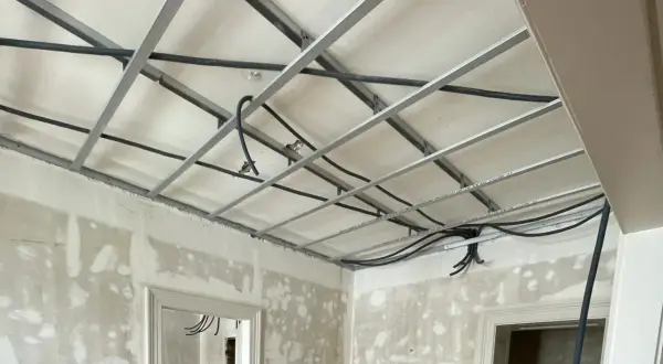 Structure métallique pour faire un faux plafond, avec des câbles électriques en cours d'installation. Les murs sont en chantier.