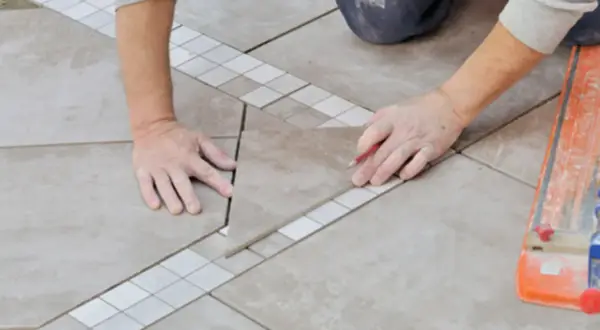 Un carreleur prépare le plan de pose du carrelage, marquant une pièce avec un crayon.