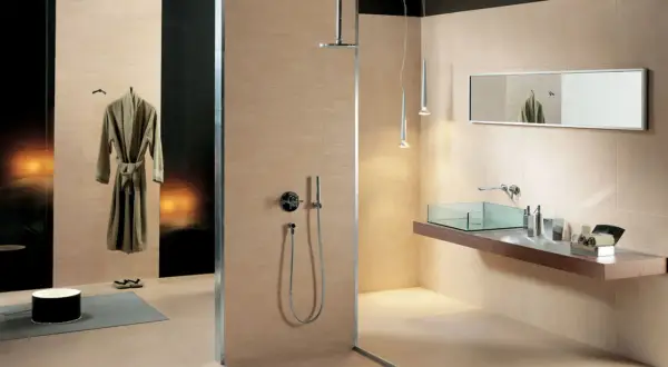Salle de bain moderne avec douche vitrée, lavabo en verre, miroir et peignoir suspendu. Les carrelages respectent la norme PEI pour une durabilité accrue.